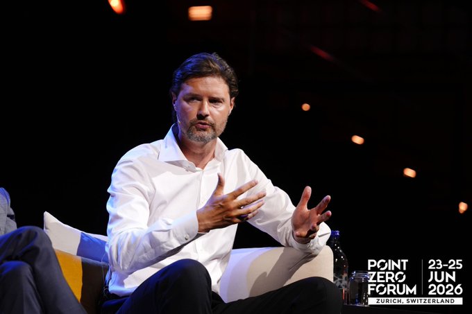A man in a white dress shirt gestures with both hands while speaking on stage, with on-screen text reading "POINT ZERO FORUM 23-25 JUN 2026 ZURICH, SWITZERLAND." The image aligns with the post's theme, visually capturing Mykolas making his point about trust as the foundation of next-generation financial platforms at the Zurich forum.