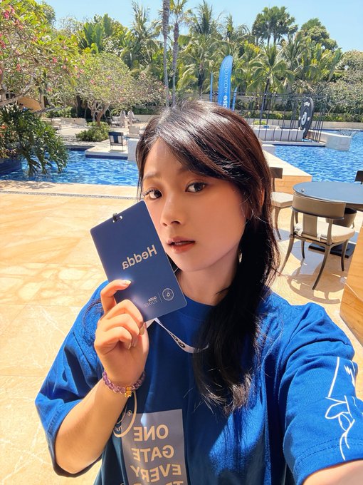 A young woman in a blue t-shirt holds up a card reading "https" and "MEGO" by a sunny pool, matching the post's "Sunshine Beach Gate" theme as she promotes Gate exchange's new multi-market stock coverage feature.
