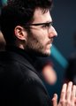 A young man with dark hair and a beard, wearing a black top, sits with his hand raised near his face in a thoughtful pose, likely a professional figure from the League of Legends esports scene possibly related to Fnatic.