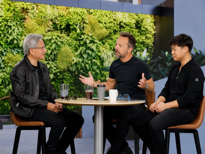 The image shows three men sitting at a table with cups of coffee and glasses, engaged in conversation. The background features a wall covered in plants, creating an atmosphere of relaxation and camaraderie among the group. The photo also includes text that reads "Is $AMD really overvalued right now? Maybe the market is not looking far enough. Goldman Sachs expects AI-agent token usage to grow 23x by 2040. Jensen Huang says inference demand could rise by a billion times. Right now, $NVDA is clearly the king of AI GPUs." The image seems to be related to an article discussing the current state and future of artificial intelligence in the technology industry.