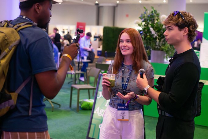 In the image, there are three people standing together in an indoor setting. One person is holding a microphone while another two individuals are engaged in conversation. The person holding the microphone appears to be talking about something related to Ethereum, as indicated by the text "me at ethconf talking about solana with a matcha". A green plant can also be seen in the background, adding some natural elements to the scene.

The people present seem to be interested in what the speaker is saying and are actively listening or waiting for their turn to speak. The setting appears to be an indoor event space where discussions about various topics might take place.