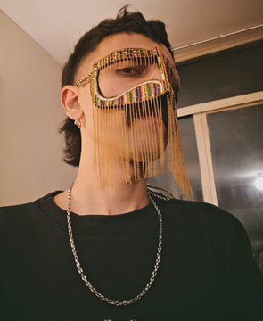 A person wearing a black t-shirt and chain necklace poses wearing large novelty sunglasses with long beaded fringe covering the face.