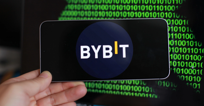 A hand holds a smartphone displaying the Bybit cryptocurrency exchange logo against a backdrop of green binary code.