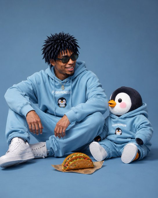 The image features two men sitting next to each other with a penguin-themed sweatshirt on one of them, and a stuffed animal penguin on the ground beside him. There's also a taco on the floor near the penguins. The caption reads "gm to everyone Waking up to a very cold morning here I think today will be a great day Got a decent point on @quipnetwork yesterday".