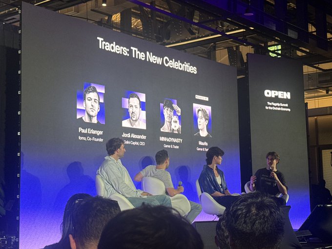 A panel discussion titled 'Traders: The New Celebrities' at an OPEN event features speakers including Paul Eitanger (Iona, Co-Founder), Jordi Alexander (Selini Capital, CEO), alongside a moderator and another panelist seated on stage.