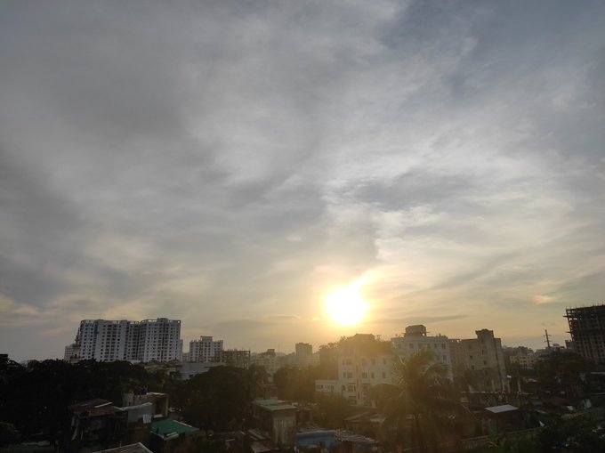 A sunset or sunrise view over a cityscape with high-rise buildings silhouetted against a cloudy sky with the sun low on the horizon.