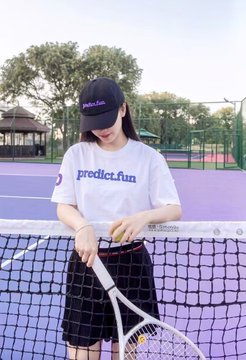 The image features a woman standing next to a tennis net, holding a tennis racket and ball. She appears to be posing for a photo or preparing to play tennis. The background of the image shows a tennis court with purple lines, indicating that this is likely an official match or practice session.