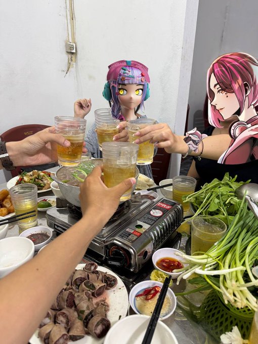 A group of people toasting with glasses of tea at a dining table with various dishes, with anime character stickers (including what appears to be Chiori from Genshin Impact) overlaid on faces.