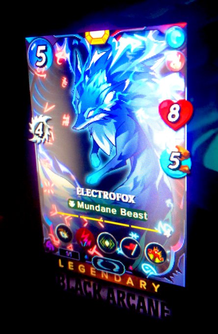 The image features a poster or display screen with a blue background, showing a game character that resembles a wolf. The game character has wings and is depicted as a blue fox. The game character's name tag reads "Electrofox" and there are several other game characters displayed on the screen. The text in the image includes phrases such as "YES! To the creator of the phrase “Welcome to the family” and the famous ANK ANGLE!!! @ANK12C pulling this card couldnt be more perfect: a @splinterlands fairy tale!".