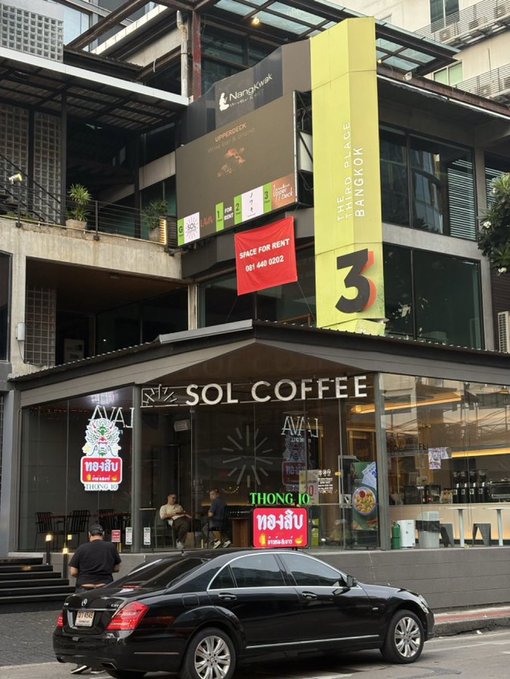 A photograph of a street-level view showing a 'SOL COFFEE' café and 'THE RISE BANGKOK 3' signage with a 'SPACE FOR RENT' banner, featuring a black Mercedes-Benz parked in front.