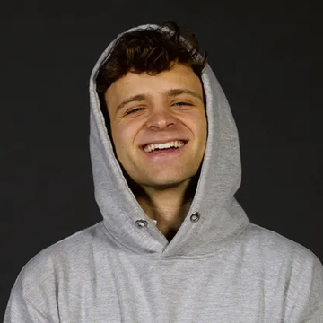 A smiling young man wearing a gray hoodie with the hood pulled up, laughing cheerfully against a black background. The image likely depicts Jack Mallers, who has stepped down as CEO of Twenty One Capital, with Raphael Zagury taking over the position.