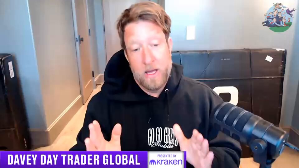 The image features a man wearing a black hoodie sitting behind a microphone, talking about Bitcoin and other digital assets. He appears to be discussing his investments or experiences with these digital currencies. The background of the image shows a room with a couch and a chair, suggesting that this conversation might take place in someone's living room.