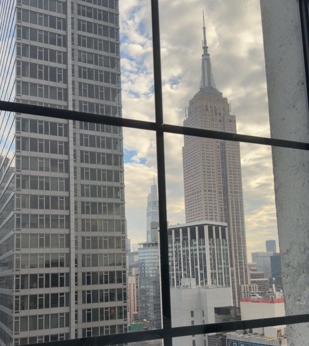A view through a window of the Empire State Building and other skyscrapers in New York City under a cloudy sky.