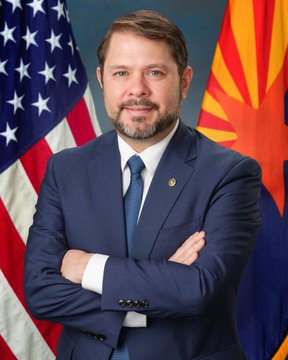 A formal portrait shows Senator Ruben Gallego in a dark blue suit with a light blue tie and an American flag lapel pin, standing with arms crossed between the U.S. flag and the Arizona state flag. The image ties directly to the post's mention of "Senator Gallego" being late with a counterproposal to the CLARITY Act's ethics provisions, as it visually identifies him as the politician being called out for delaying crypto legislation.