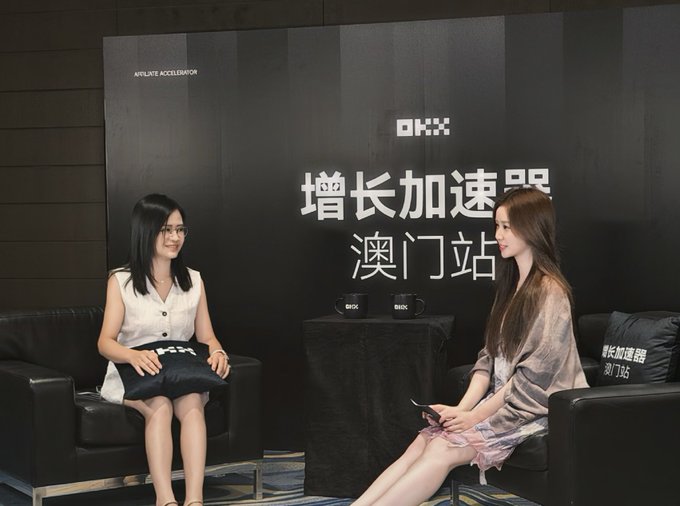 Two women seated on black leather chairs in an interview setup, with Chinese text '增长加速器 澳门站' (Growth Accelerator Macau Station) and the OKX logo on the backdrop.