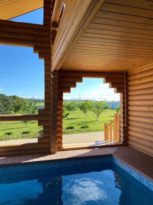 The view from a covered wooden patio looks out over a green landscape and an indoor pool in the foreground.