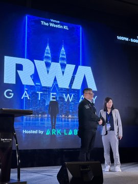 Two people standing on stage at the 'RWA Gateway' event at The Westin KL, hosted by ARK LAB, with a large screen displaying the event branding behind them.