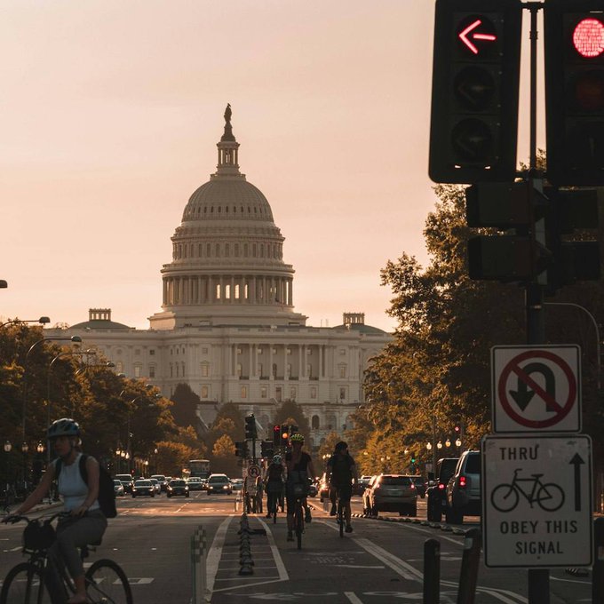 A sunset view of the U.S. Capitol building in Washington D.C., with cyclists on the street and a 'No U-turn / Thru Obey This Signal' traffic sign in the foreground.