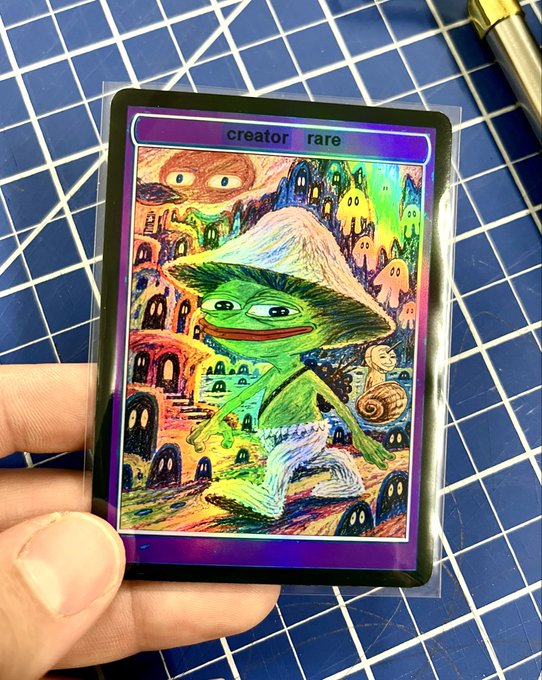 A hand holding a holographic trading card featuring a colorful illustrated green frog-like character wearing a large hat, with the text 'creator rare' at the top.