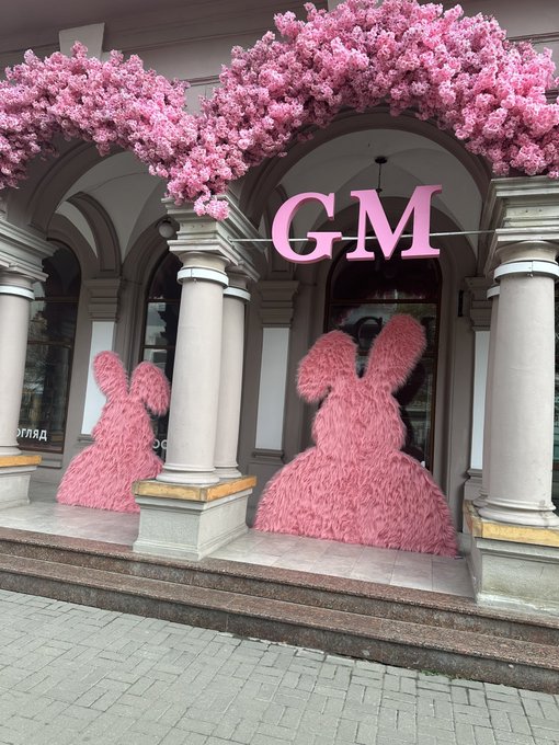 An elegant building facade is decorated with abundant pink cherry blossoms and large pink bunny silhouettes flanking the entrance, with 'GM' displayed prominently.