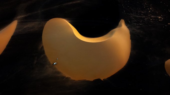 An abstract, glowing crescent shape in golden-orange tones set against a dark, textured background.