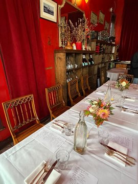 A long dining table set with white linens, wine glasses, and floral centerpieces stretches through an intimate restaurant with red walls and wooden chairs, ready to host the tech-themed dinner where guests discussed OTC deals and datacenter colocation.