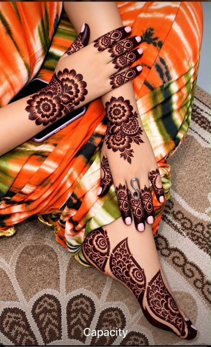 A close-up shows hands and feet adorned with intricate dark brown henna (mehndi) designs, resting against an orange and green patterned fabric, with the word 'Capacity' written at the bottom.