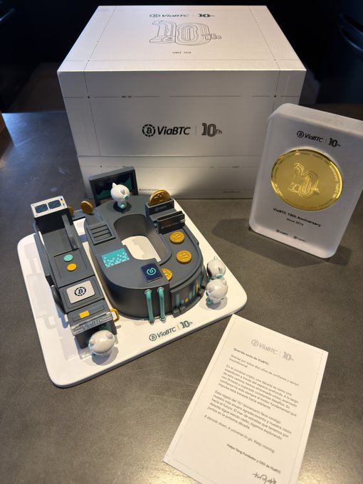 A 10th anniversary commemorative display from ViaBTC features a detailed miniature mining rig diorama, a gold coin dated "2014–2024," and a thank-you letter, celebrating the company's decade in the cryptocurrency mining industry.