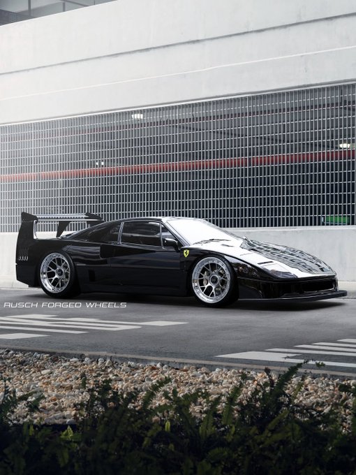 A black Ferrari F40 sports car with custom Rusch Forged Wheels is parked on a street in front of a modern industrial building.