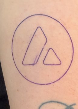 A close-up shows a purple ink tattoo of two triangles inside a circle on someone's skin.