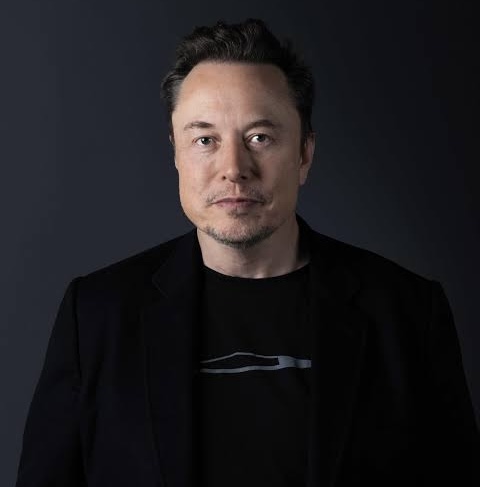 A professional headshot of Elon Musk, dressed in a black blazer over a dark shirt, looking directly at the camera against a dark gray background. The image accompanies the post's breaking news about Musk's plan to pay original X content creators in a crypto stablecoin.