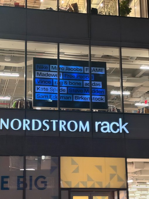 A storefront sign reads 'NORDSTROM rack' with a window display above listing brand names including Marc Jacobs, FAME, Madewell, Free People, Vince, rag & bone, adidas, Kate Spade, Steve Madden, Sam Edelman, and Birkenstock.