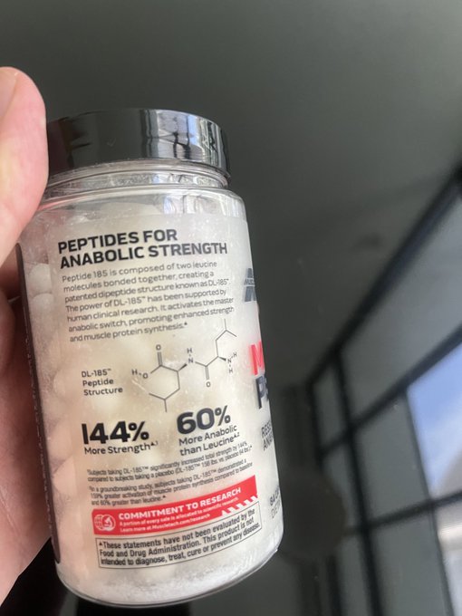 A hand holding a bottle of 'Peptides for Anabolic Strength' featuring DL-185 Peptide, with claims of 144% more strength and 60% more anabolic than Leucine.