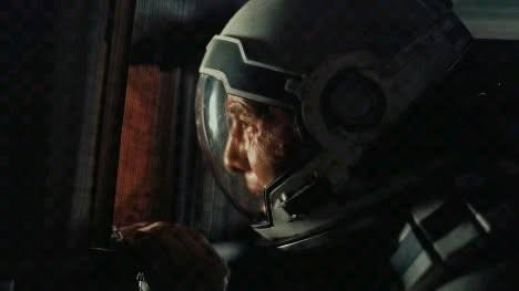 A close-up shot of an astronaut's face visible through the visor of their helmet, showing signs of distress or scarring.