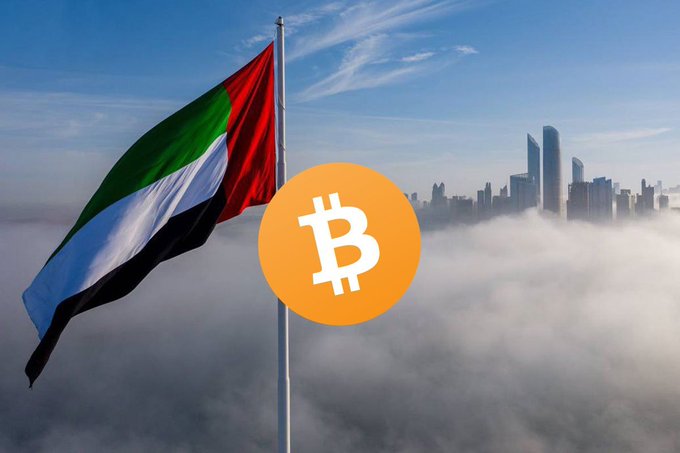 The flag of the United Arab Emirates waves in the foreground with a Bitcoin logo overlay, set against a foggy cityscape with skyscrapers.