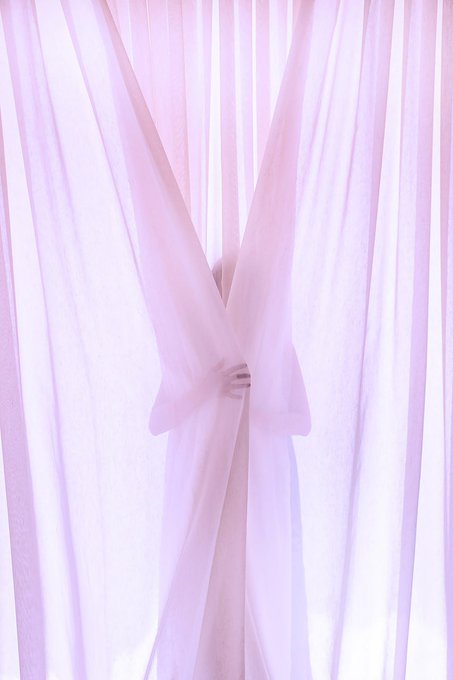 A person stands behind flowing pink and white sheer curtains, with only their hands visible as they grasp the fabric, creating an ethereal, minimalist composition.
