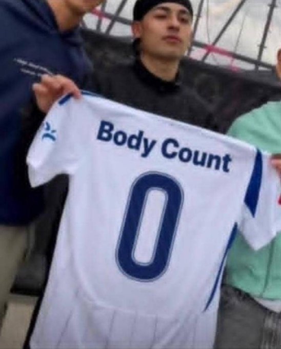 Two people hold up a white soccer jersey with the text 'Body Count' and the number '0' printed on the back in blue.