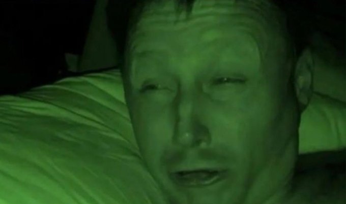 A close-up night-vision selfie captures a man's tired, sweaty face squinting into the camera in a dark, low-light setting. The image's groggy, half-awake expression humorously reinforces the post's sarcastic tone of "winning," suggesting exhaustion rather than triumph.