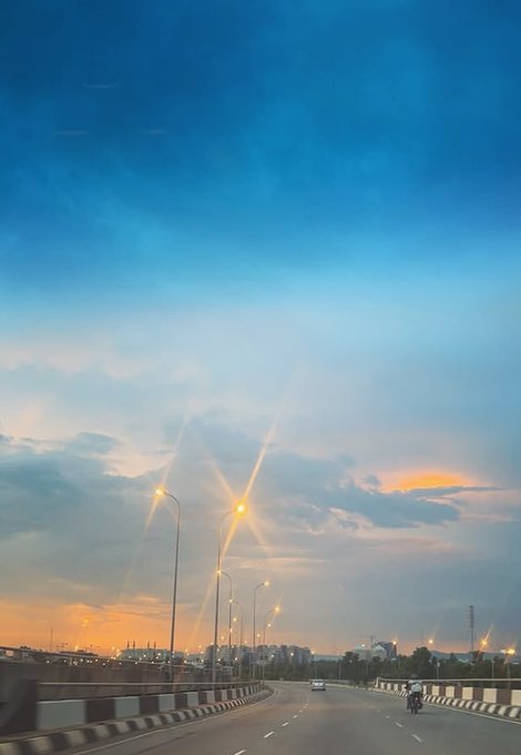 The image shows a highway with two lanes of traffic, one lane being used by a motorcycle and the other by cars. There are also street lights along the road. In the background, there's an orange sky that appears to be sunset or sunrise, creating a beautiful atmosphere over the scene. The post about adoption seems unrelated to the image but is placed in the top right corner of the photo.
