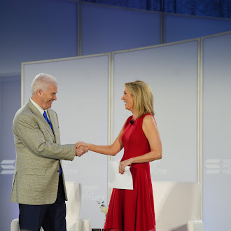A man in a tan checkered suit shakes hands with Kristin Smith, president of the Solana Policy Institute, who wears a red dress and holds papers, on a stage during what appears to be a digital assets policy discussion. The image captures the friendly meeting referenced in the post about advancing U.S. leadership in digital assets innovation.