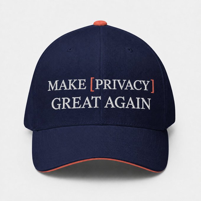 A navy blue baseball cap with orange trim displays the embroidered text "MAKE [PRIVACY] GREAT AGAIN" in white and orange lettering, with "PRIVACY" highlighted in brackets. The cap's design aligns with the post's message, presenting a fashion-forward take on the privacy advocacy slogan.