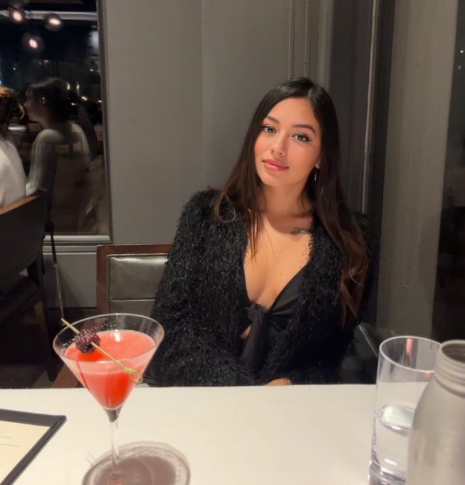A young woman with long dark hair sits at an upscale restaurant table, smiling softly at the camera with a pink berry-garnished martini in front of her. The elegant dinner setting visually complements the post's theme of celebrating SOL reaching $109.