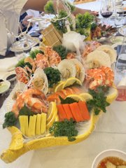 A seafood platter featuring shrimp, crab, and vegetables garnished with lemon, served on a golden tray with a small bowl of sauce.