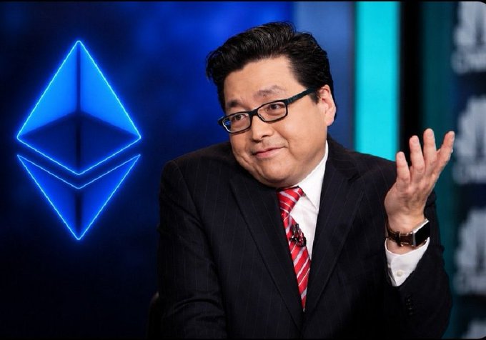 The image features a man wearing glasses, suit, and tie giving a thumbs up sign while standing against a blue background with an Ethereum logo behind him. The caption states that there's another $60 million worth of Bitcoin on his balance sheet which might be a part of a Bullish stance he is expressing through his gesture. This could imply his excitement about the recent addition to his portfolio or the potential value of Bitcoin and the blockchain technology in general.