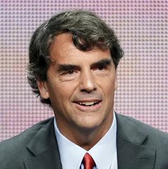 A close-up headshot of economist and TV personality Nouriel Roubini, wearing a dark suit and red tie.