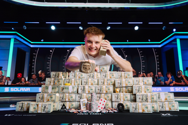 A poker player celebrating at a final table with stacks of cash, poker chips, and a championship belt, with 'SOLANA' branding visible on the table.