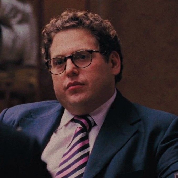 A man with curly hair and aviator-style glasses, wearing a blue suit with a pink and navy striped tie, sits with a serious, contemplative expression in what appears to be a formal meeting setting. The image pairs with the post "Be sincere - When last did you P2P?" to reflect on peer-to-peer financial transactions, with the man's pensive demeanor mirroring the call for honest reflection on one's recent P2P activity.