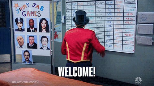 The image features a man dressed as a clown standing next to a whiteboard with the words "Welcome!" written on it. The clown appears to be wearing a red jacket and top hat, adding a whimsical touch to his appearance. The background of the image includes several photos of people, which could potentially be related to the clown's performance or event he is attending.