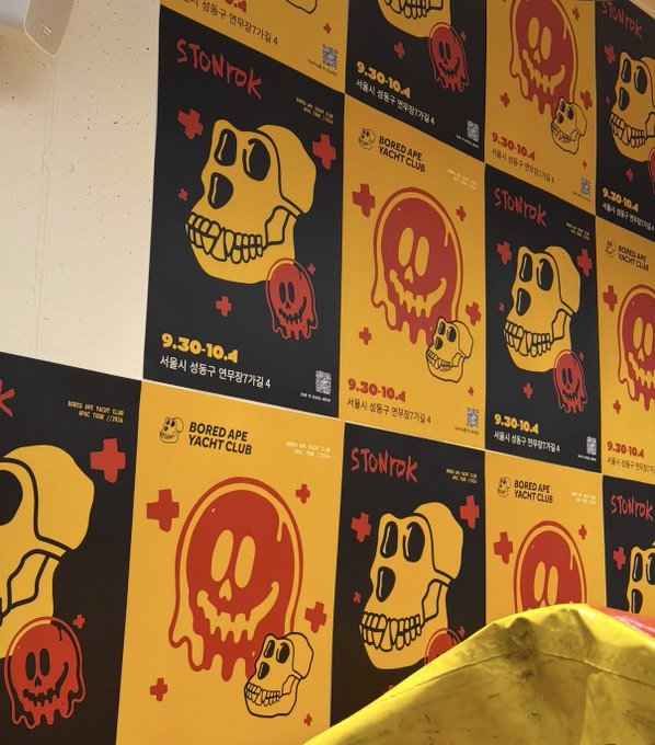 A wall covered in repeating promotional posters for a 'STONtrök' x 'BORED APE YACHT CLUB' event taking place from '9.30-10.4' in Seoul, featuring yellow and red cartoon skull graphics.