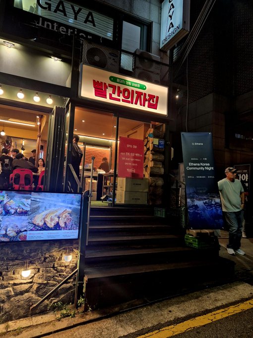 A nighttime photo of a Korean restaurant storefront with a red sign reading "빌군의자집" (Bil-gun's House of Chairs) on GAYA interior's second floor, featuring promotional posters for grilled fish and an Ethena Korea Community Night event.